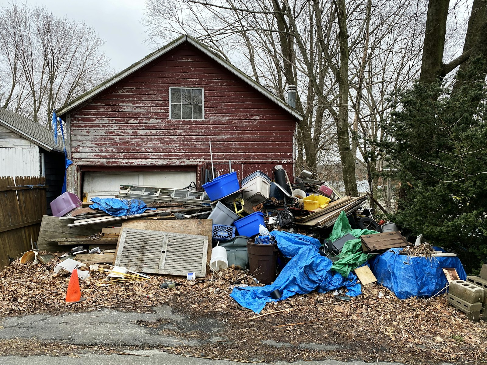 A large pile of miscellaneous household junk and debris piled up in front of a red garage.